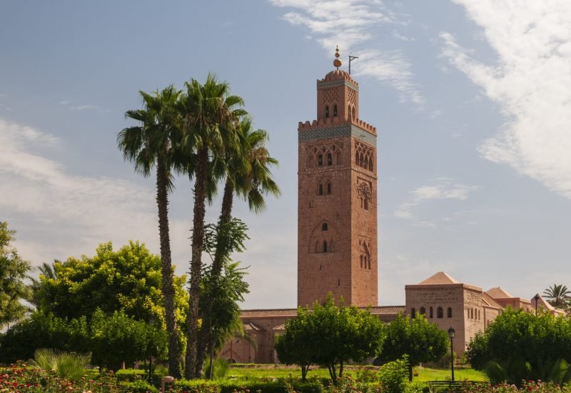 An iconic Moroccan minaret towers over lush gardens under a clear blue sky.