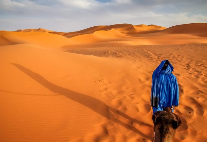 Berber leading a camel into the stunning sand dunes of Sahara desert in Merzouga, Morocco