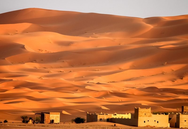 Berber homes at the foot of gigantic and stunning sand dunes of Sahara desert in Merzouga, Morocco
